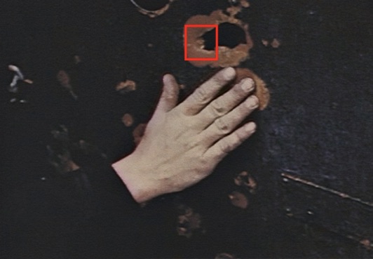 Figure 5. A close examination of this hole reveals gouge marks on the left/forward edge of the puncture. This would indicate the shell fragment struck at an angle to the face of the shelf. Still from David T. Ruley film clip.